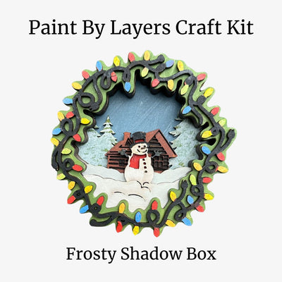 Paint by Layers Craft Kit for Frosty Shadow Box with a snowman and cabin design.