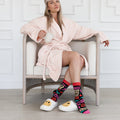 Woman in a pink robe sitting on a chair wearing colorful socks with text and patterns.