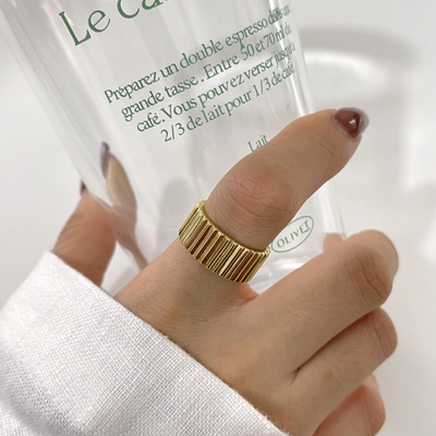 A wide band gear ring made with 18k gold fill, featuring a textured design resembling interlocking gears, worn on a person's thumb while holding a glass. This statement ring is available in Ottawa, Ontario, Canada.