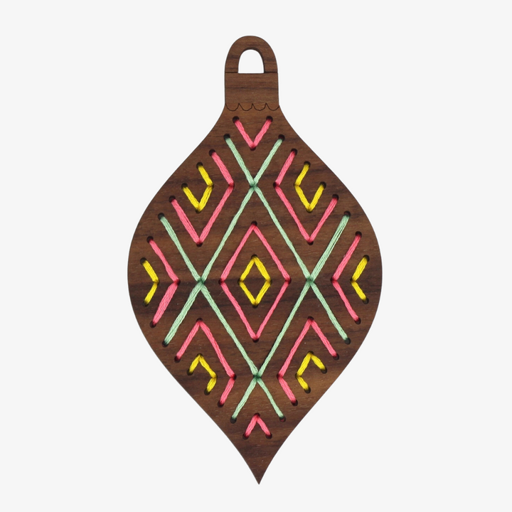 A wooden ornament shaped like a teardrop. The ornament is decorated with colorful embroidery stitches in a geometric diamond pattern.