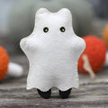 White ghost plush toy with black eyes on a wooden surface with colorful background
