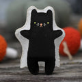 Black cat plush toy with ghost outline on a wooden surface with colorful pumpkins in the background