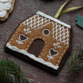 Decorative gingerbread house ornament on a wooden surface with greenery