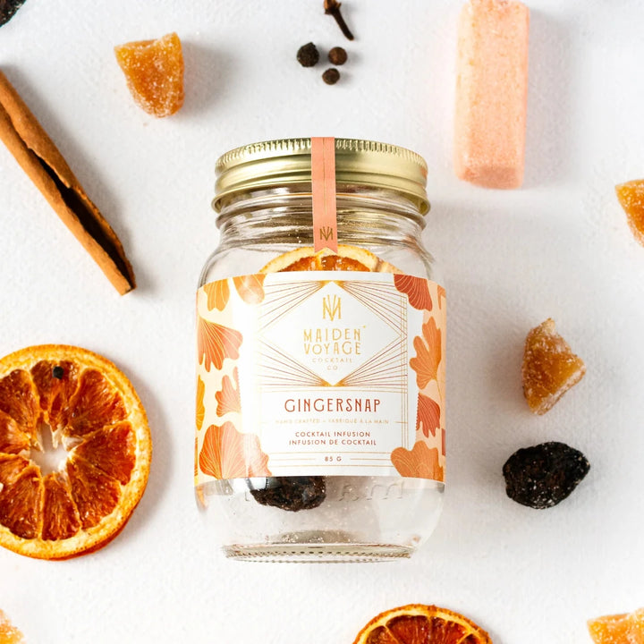 A glass jar filled with dried orange slices, cloves, and other spices. The jar has a white label with the Maiden Voyage logo and the product name 