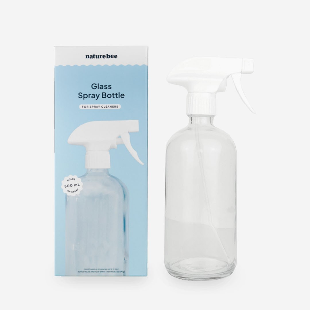 Clear glass spray bottle with white nozzle next to its packaging on a white background