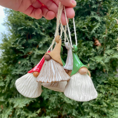 Hand holding three small gnome figurines against a green tree background