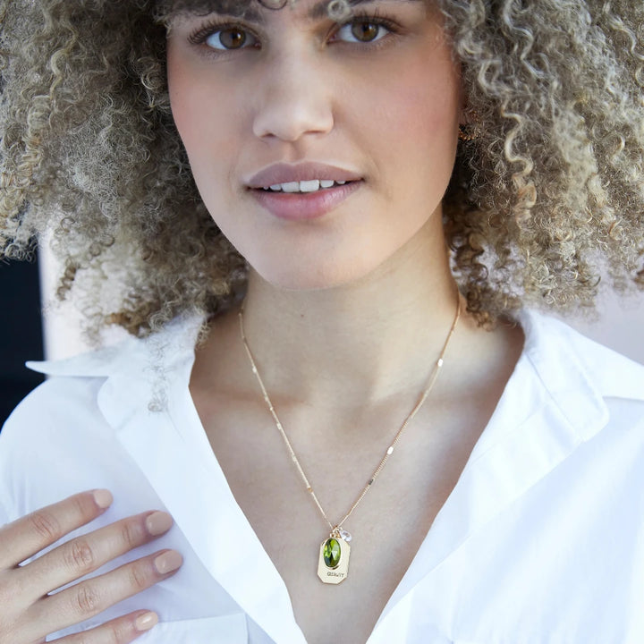 A gold necklace with a peridot stone pendant. The pendant also has the word 