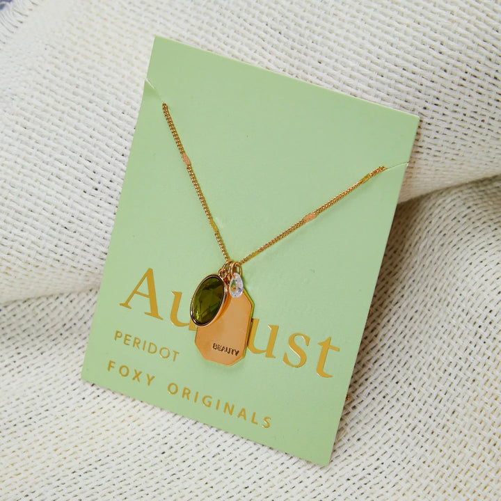 A gold necklace with a peridot stone pendant. The pendant also has the word 
