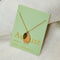 A gold necklace with a peridot stone pendant. The pendant also has the word 