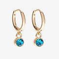 A set of three pairs of turquoise earrings displayed on a blue card. The set includes a pair of stud earrings, a pair of bar earrings with small turquoise beads, and a pair of hoop earrings with dangling turquoise stones. The card has the month "December" and the brand name "Foxy Originals."