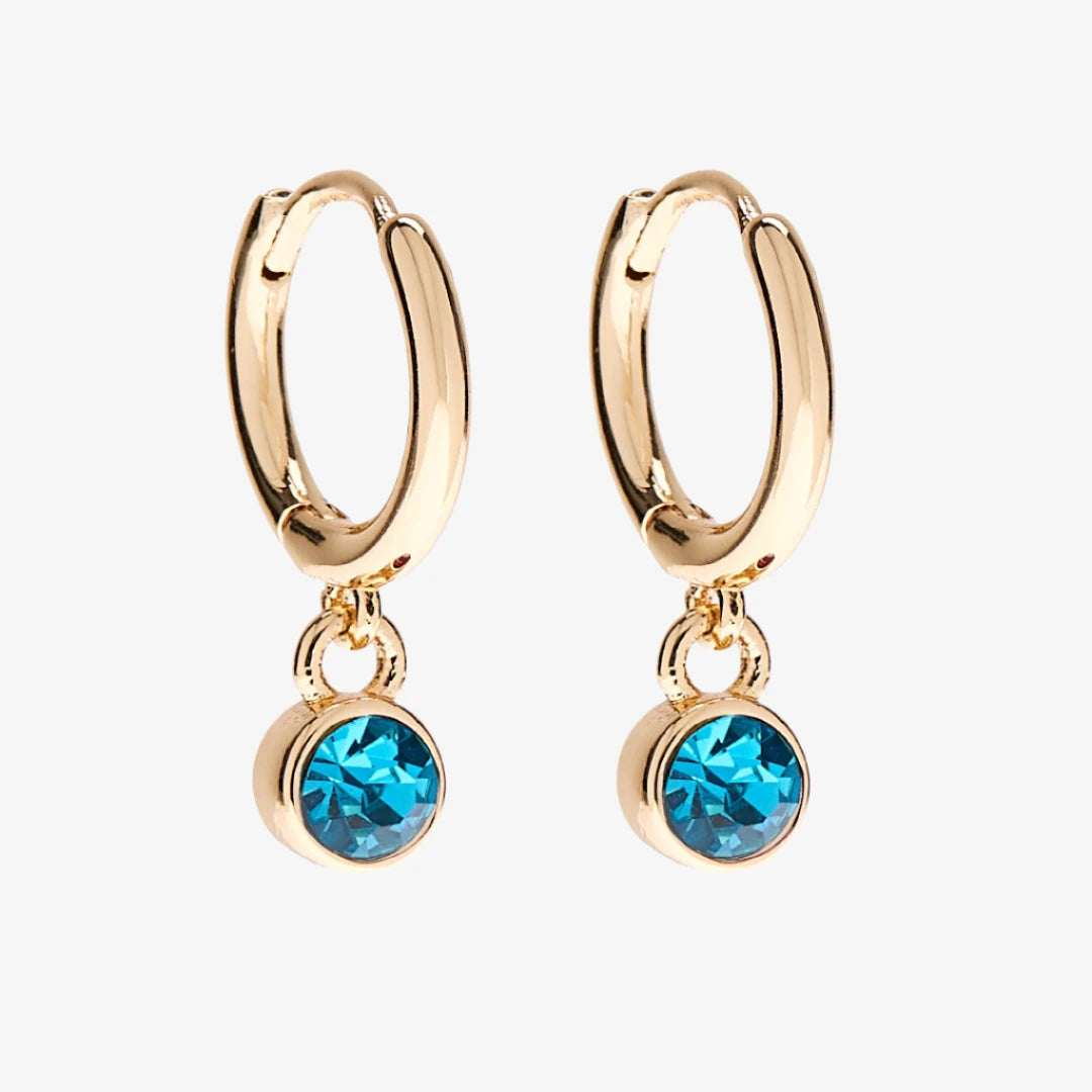 A set of three pairs of turquoise earrings displayed on a blue card. The set includes a pair of stud earrings, a pair of bar earrings with small turquoise beads, and a pair of hoop earrings with dangling turquoise stones. The card has the month "December" and the brand name "Foxy Originals."