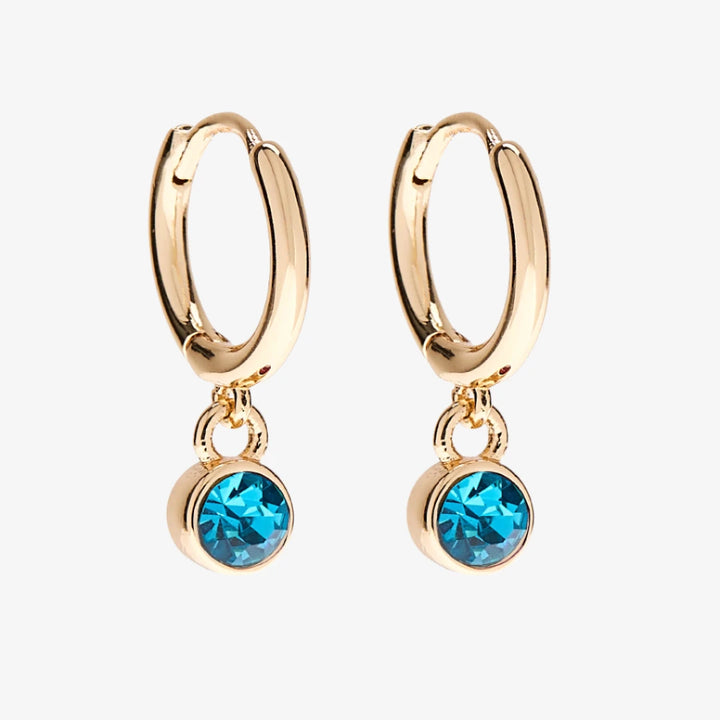 A set of three pairs of turquoise earrings displayed on a blue card. The set includes a pair of stud earrings, a pair of bar earrings with small turquoise beads, and a pair of hoop earrings with dangling turquoise stones. The card has the month 
