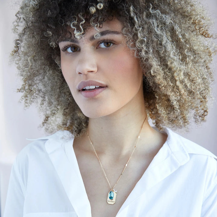 A gold necklace with a turquoise stone pendant. The pendant also has the word 