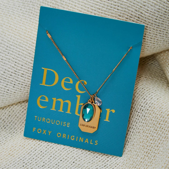 A gold necklace with a turquoise stone pendant. The pendant also has the word 