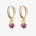 A set of three pairs of amethyst earrings displayed on a purple card. The set includes a pair of stud earrings, a pair of bar earrings with small amethyst beads, and a pair of hoop earrings with dangling amethyst stones. The card has the month "February" and the brand name "Foxy Originals."