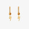 A pair of gold earrings with lightning bolt charms on a pink background. The earrings are displayed on a card with the brand name 
