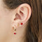 A set of three pairs of ruby earrings displayed on a red card. The set includes a pair of stud earrings, a pair of bar earrings with small ruby beads, and a pair of hoop earrings with dangling ruby stones. The card has the month 