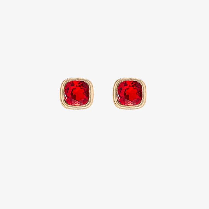 A set of three pairs of ruby earrings displayed on a red card. The set includes a pair of stud earrings, a pair of bar earrings with small ruby beads, and a pair of hoop earrings with dangling ruby stones. The card has the month 