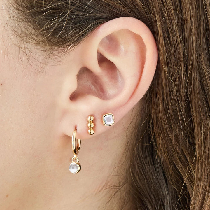 A set of three pairs of pearl earrings displayed on a blue card. The set includes a pair of stud earrings, a pair of bar earrings with small pearl beads, and a pair of hoop earrings with dangling pearl stones. The card has the month 