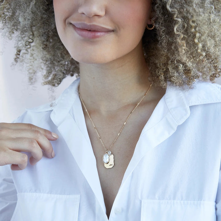 A gold necklace with a pearl stone pendant. The pendant also has the word 
