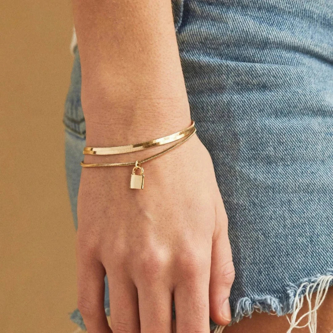 A gold layered bracelet with a small padlock charm. The bracelet has two chains of different widths, and the padlock charm hangs from the thinner chain.