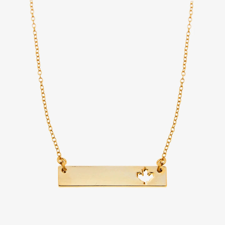 A gold necklace with a bar pendant. The bar has a cut-out maple leaf design.
