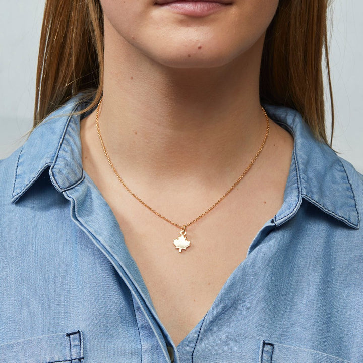 A gold necklace with a maple leaf pendant.