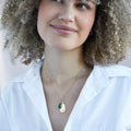 A gold necklace with an emerald stone pendant. The pendant also has the word "HOPE" engraved on it. The necklace is displayed on a green card with the month "May" and the brand name "Foxy Originals."