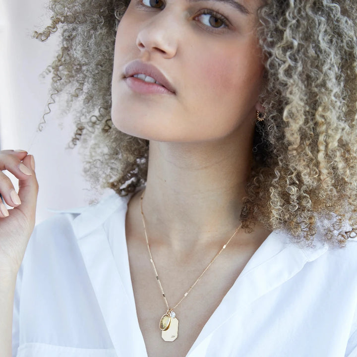 A gold necklace with a citrine stone pendant. The pendant also has the word 