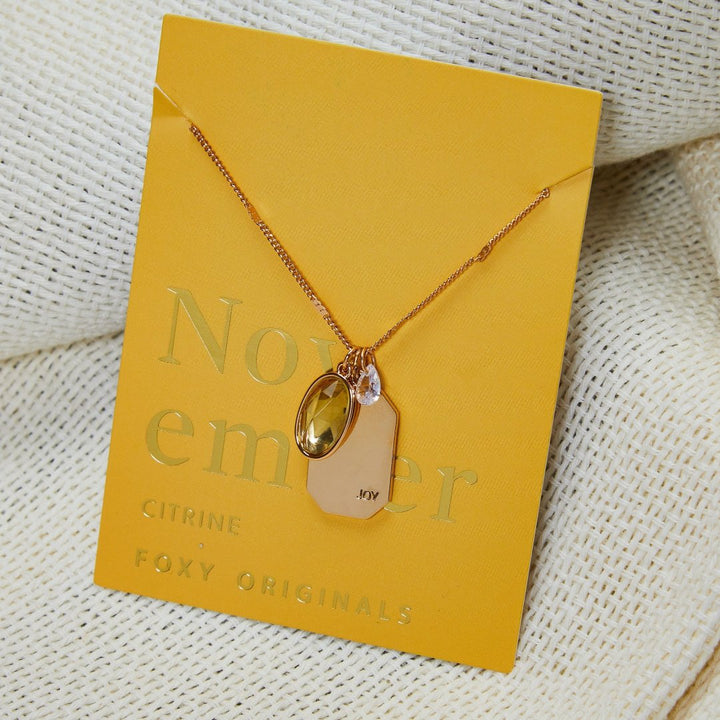 A gold necklace with a citrine stone pendant. The pendant also has the word 