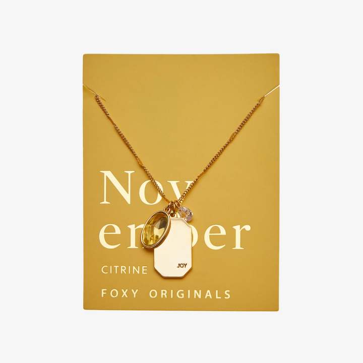 A gold necklace with a citrine stone pendant. The pendant also has the word 