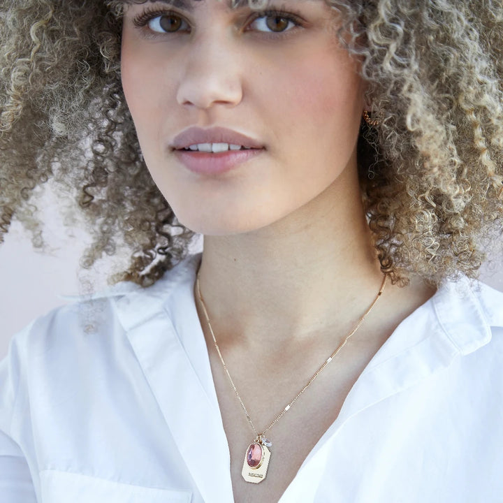 A gold necklace with an opal stone pendant. The pendant also has the word 