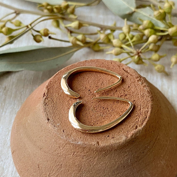 A pair of Agaveh Girl Gold Aspyn Hoops, featuring a minimalist, open curved design, displayed on a branded card with the text 'agaveh girl,' against a textured background. The earrings are dainty and modern, available in Ottawa, Ontario, Canada.