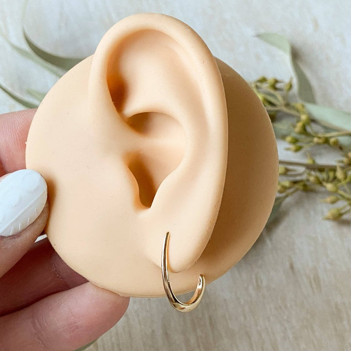 A pair of Agaveh Girl Gold Aspyn Hoops, featuring a minimalist, open curved design, displayed on a branded card with the text 'agaveh girl,' against a textured background. The earrings are dainty and modern, available in Ottawa, Ontario, Canada.