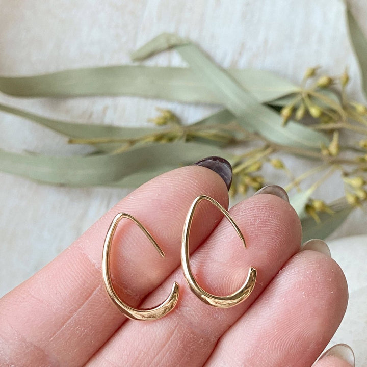 A pair of Agaveh Girl Gold Aspyn Hoops, featuring a minimalist, open curved design, displayed on a branded card with the text 'agaveh girl,' against a textured background. The earrings are dainty and modern, available in Ottawa, Ontario, Canada.
