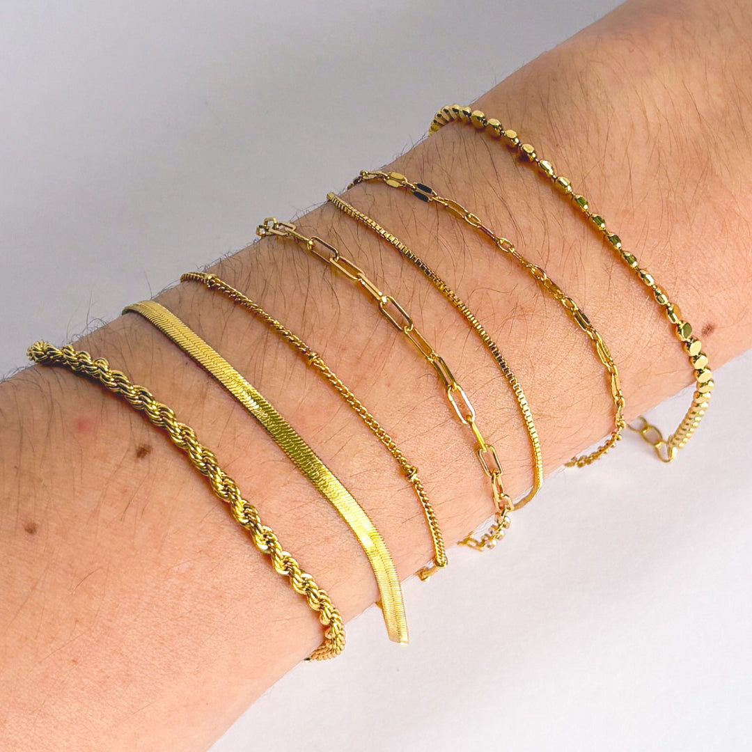 Gold bracelets on a wrist against a neutral background