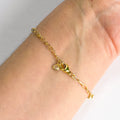 Gold bracelet with a small heart charm on a wrist against a neutral background