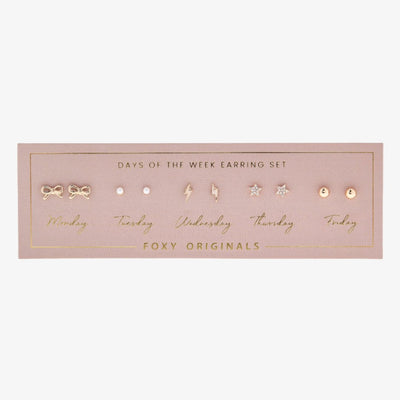 A set of gold stud earrings representing the days of the week. The earrings are arranged on a pink card with the words 