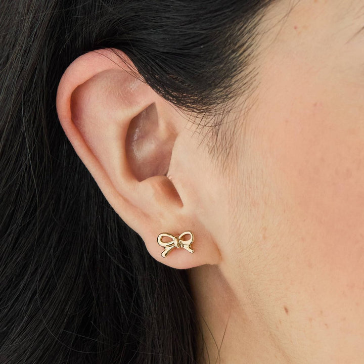 A set of gold stud earrings representing the days of the week. The earrings are arranged on a pink card with the words 