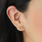 A set of gold stud earrings representing the days of the week. The earrings are arranged on a pink card with the words 