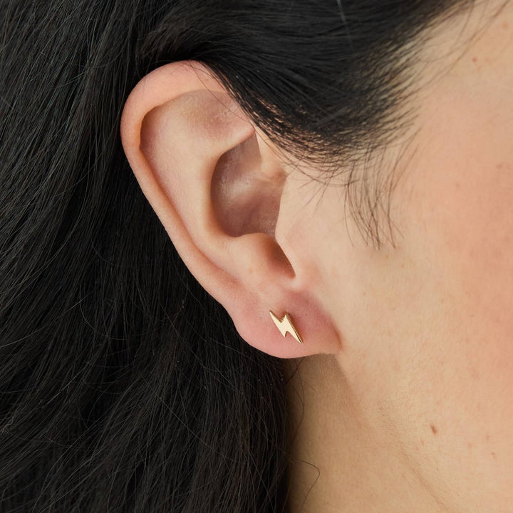 A set of gold stud earrings representing the days of the week. The earrings are arranged on a pink card with the words 