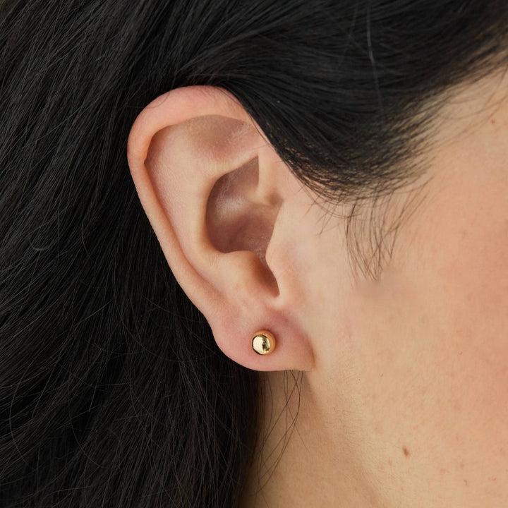 A set of gold stud earrings representing the days of the week. The earrings are arranged on a pink card with the words 