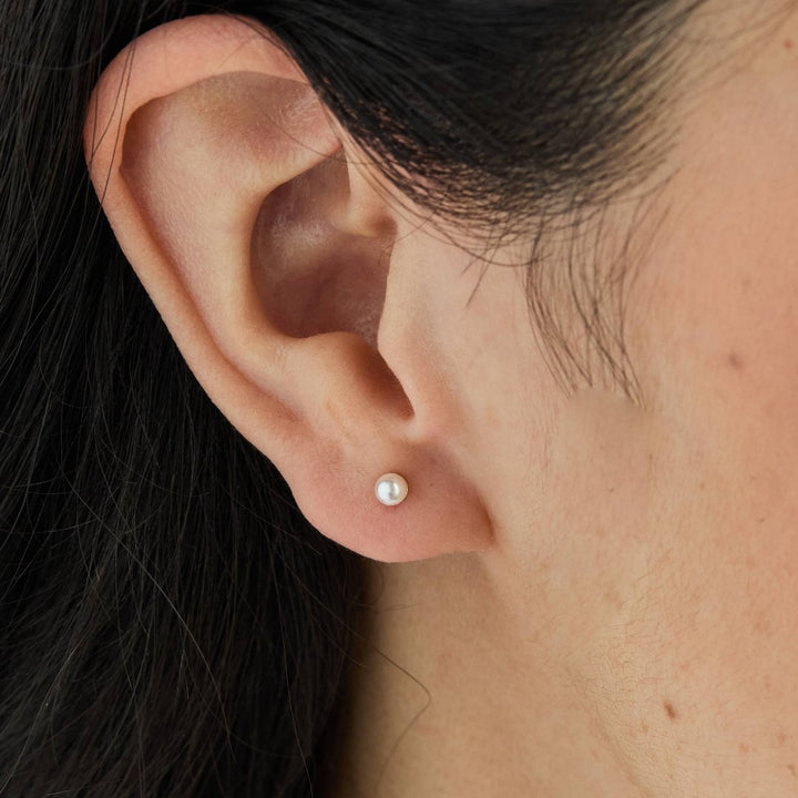 A set of gold stud earrings representing the days of the week. The earrings are arranged on a pink card with the words 