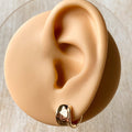 A pair of gold Grace hoops, featuring a chunky, domed design, displayed on a textured wooden surface with white floral accents. The earrings are statement huggie hoops, available in Ottawa, Ontario, Canada.