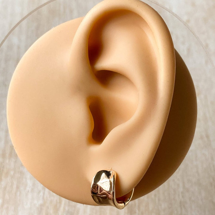 A pair of gold Grace hoops, featuring a chunky, domed design, displayed on a textured wooden surface with white floral accents. The earrings are statement huggie hoops, available in Ottawa, Ontario, Canada.