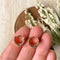 A pair of gold Grace hoops, featuring a chunky, domed design, displayed on a textured wooden surface with white floral accents. The earrings are statement huggie hoops, available in Ottawa, Ontario, Canada.