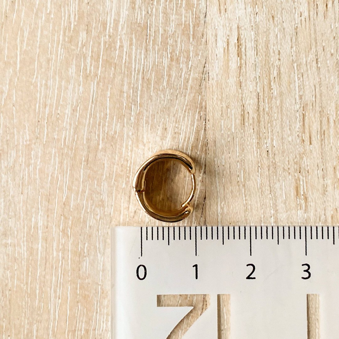 A pair of gold Grace hoops, featuring a chunky, domed design, displayed on a textured wooden surface with white floral accents. The earrings are statement huggie hoops, available in Ottawa, Ontario, Canada.