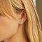 A pair of gold stud earrings with multiple rectangular crystals on a pink card with the brand name 