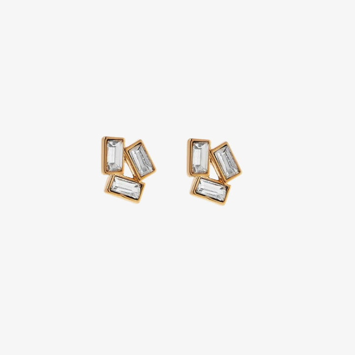 A pair of gold stud earrings with multiple rectangular crystals on a pink card with the brand name 