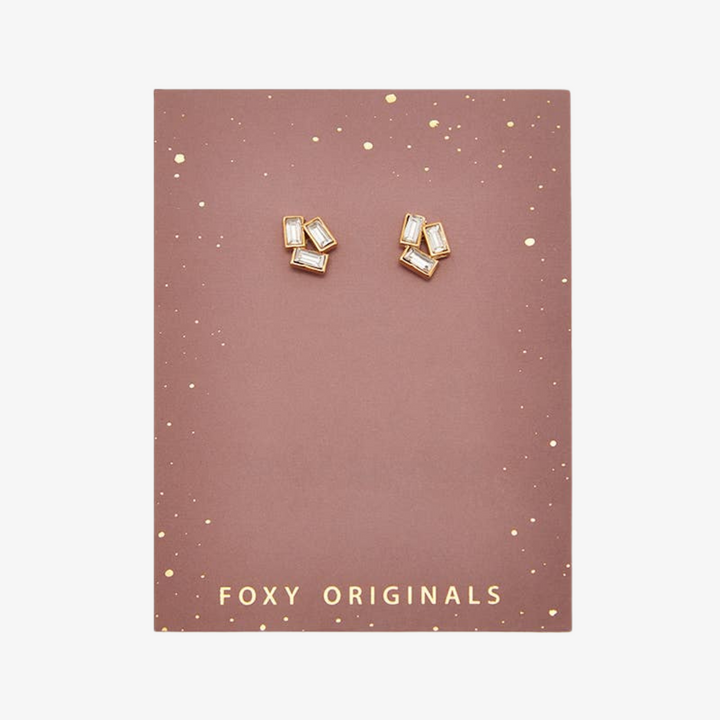 A pair of gold stud earrings with multiple rectangular crystals on a pink card with the brand name 